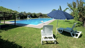A swimming pool with a blue umbrella, white lounge chairs, and a grassy area.