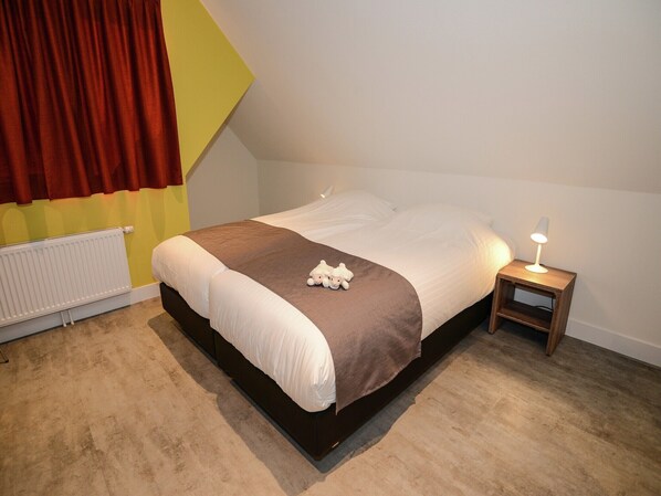 A bedroom with a bed, a bedside table with a lamp, a radiator, and a window with curtains.