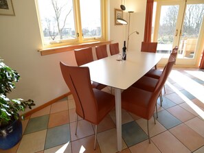 A dining area with a white table and brown chairs, large windows, and a potted plant. - Mansion in De Cocksdorp (De Cocksdorp-Texel)