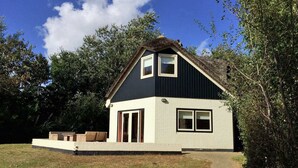 A two-story house with a dark roof, light walls, and a small porch with seating.