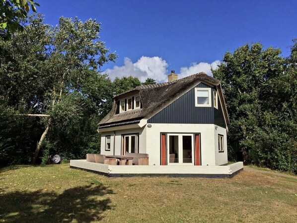 A two-story house with a thatched roof, a small balcony, and a paved patio area. - Mansion in De Cocksdorp (De Cocksdorp-Texel)