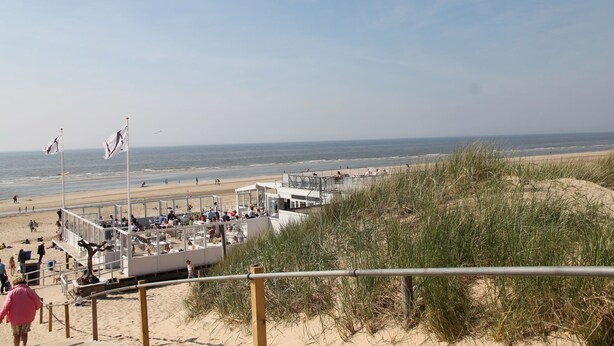 Un restaurante frente a la playa con terraza al aire libre, vista al océano, una playa de arena y dunas al fondo.