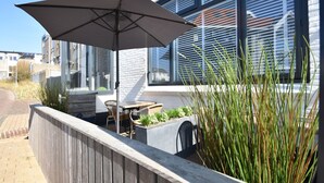 Un patio al aire libre con una mesa, sillas, un paraguas grande y una jardinera con plantas.