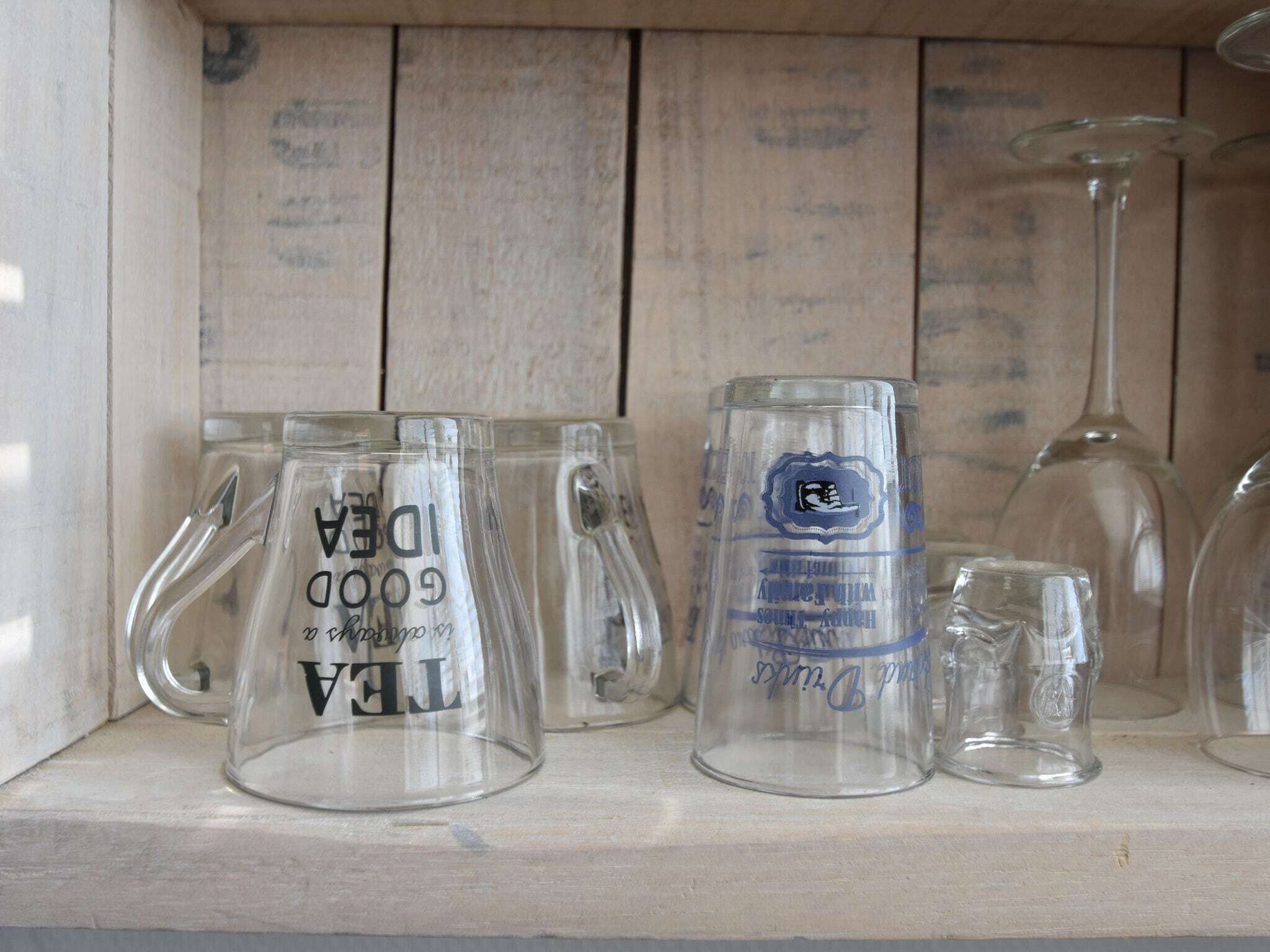 A shelf with various glass items, including mugs and a wine glass.