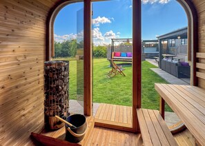 A sauna room with a wooden interior, a sauna tub, and a view of an outdoor patio area with a barbecue and seating. - Spa Utopia (Sauna & Hot tub) (Raywell, Beverley)