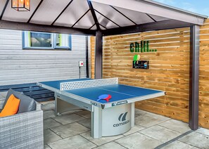 An outdoor table tennis table with a net, a ping pong paddle, and a wall with a 'chill...' sign.