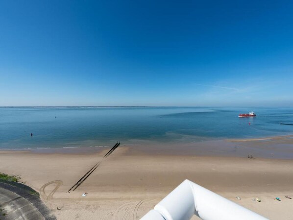 A beach with a clear sky, calm sea, and a distant red boat.