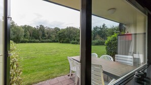 Un patio con una mesa y sillas, vista a un jardín cubierto de césped y una terraza de madera.