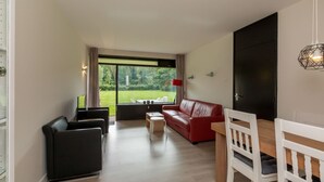 Una sala moderna con un sofá rojo, una mesa de comedor con sillas blancas y un ventanal con vistas a un paisaje verde.