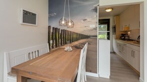 Un comedor con una mesa y sillas de madera, un mural con escena de playa y vistas a una cocina moderna.