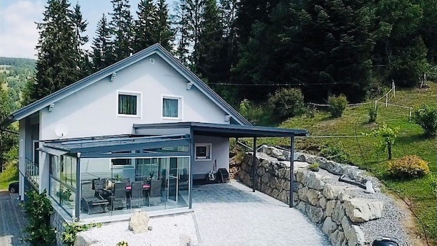 A modern house with a glass-enclosed patio, stone walls, and a view of a forested hillside. - Apartment in Salchau near Lachtal Ski Area (Salchau)