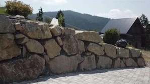 A stone wall with a paved area in front, a wooden cabin, and a mountainous backdrop. - Apartment in Salchau near Lachtal Ski Area (Salchau)