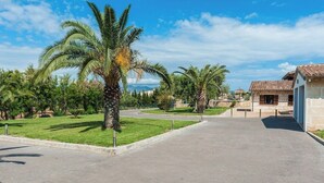 A paved pathway leading to a building with a tiled roof, surrounded by palm trees and greenery. - Villa with private pool in a privileged environment. Wifi, A/c & lovely BBQ (Alcúdia)