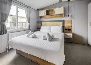 A modern hotel room with a large bed, a wooden headboard, a bedside table, and a built-in shelf above the bed.