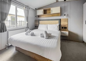 A modern hotel room with a large bed, a wooden headboard, a bedside table, and a built-in shelf above the bed.