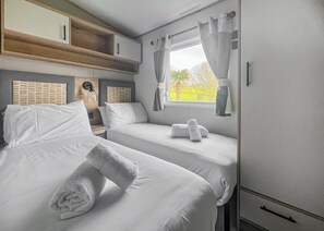 Un dormitorio con dos camas, una ventana con cortinas, una mesita de noche con lámpara y un armario.