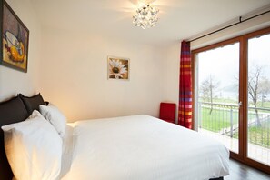 A bedroom with a large bed, a window with a view, a painting on the wall, and a chandelier.