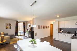 A modern living room with a dining table, sofa, and a kitchen area with white cabinets and a black countertop.