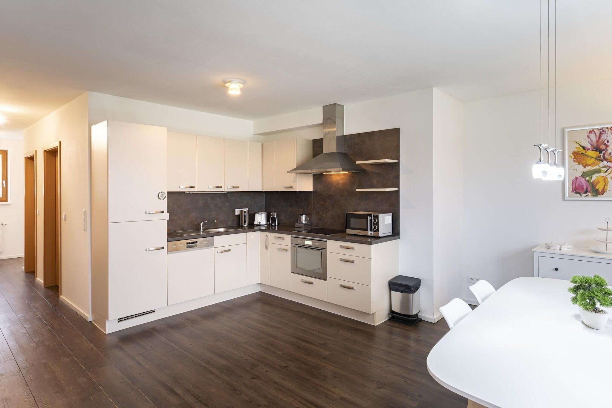 Una cocina moderna con armarios blancos, una campana extractora de acero inoxidable y un comedor con mesa y sillas blancas.