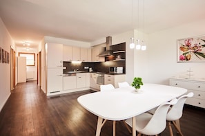 A modern kitchen with white cabinets, a dining table with chairs, and a hanging light fixture.