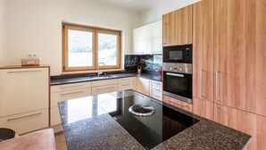 Een moderne keuken met een zwart inductiekookveld, roestvrijstalen apparatuur en houten kastjes.