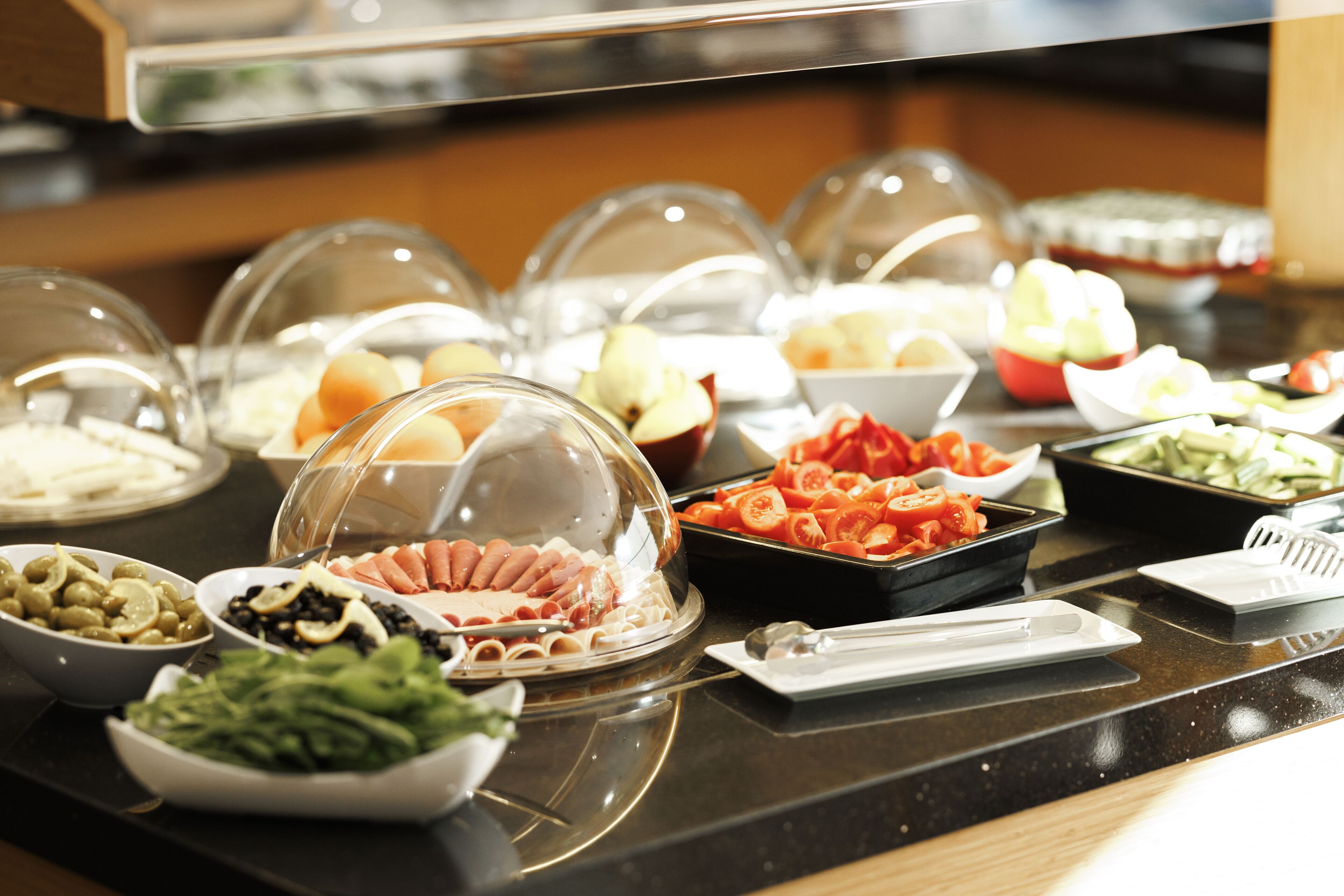 A buffet with various food items under glass domes, including meats, vegetables, and fruits.