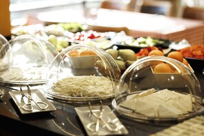 A buffet with various food items under glass domes, including cheese, fruits, and vegetables.
