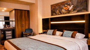 Une chambre d’hôtel avec un grand lit, un bureau avec une machine à café, une chaise et un tableau au mur.
