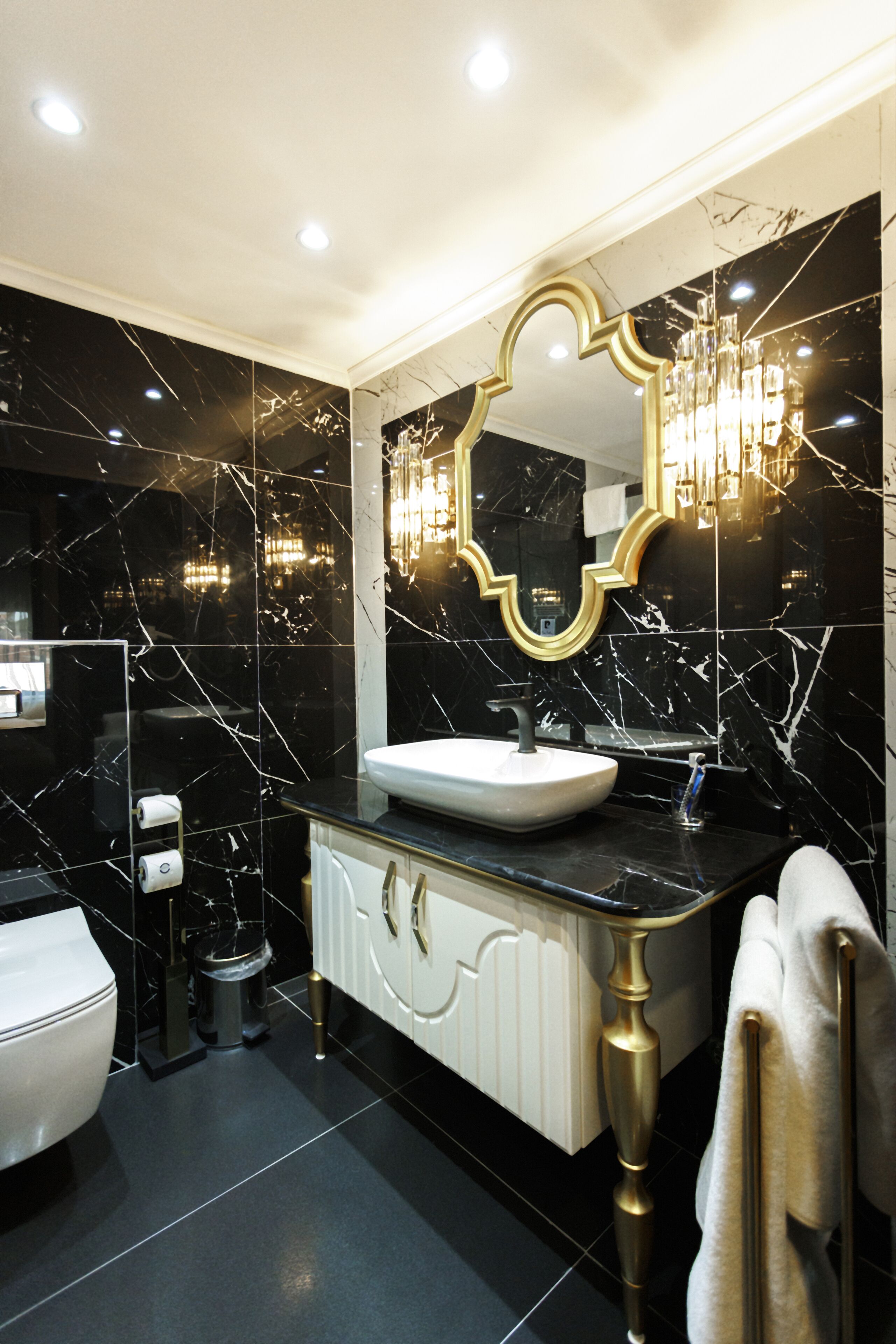 A modern bathroom with a black marble wall, a white sink, and a gold-framed mirror.