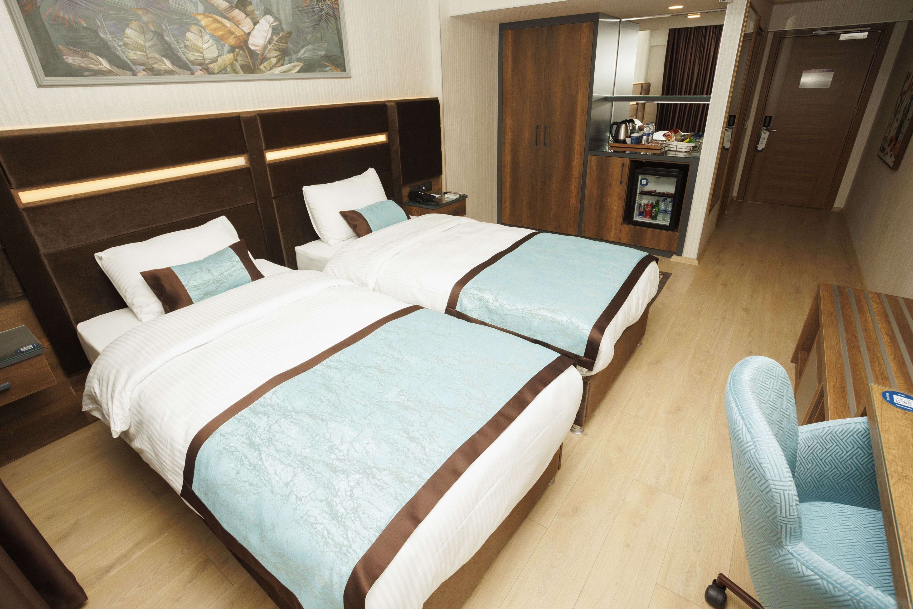 A hotel room with two beds, a desk, a chair, a minibar, and a wardrobe.