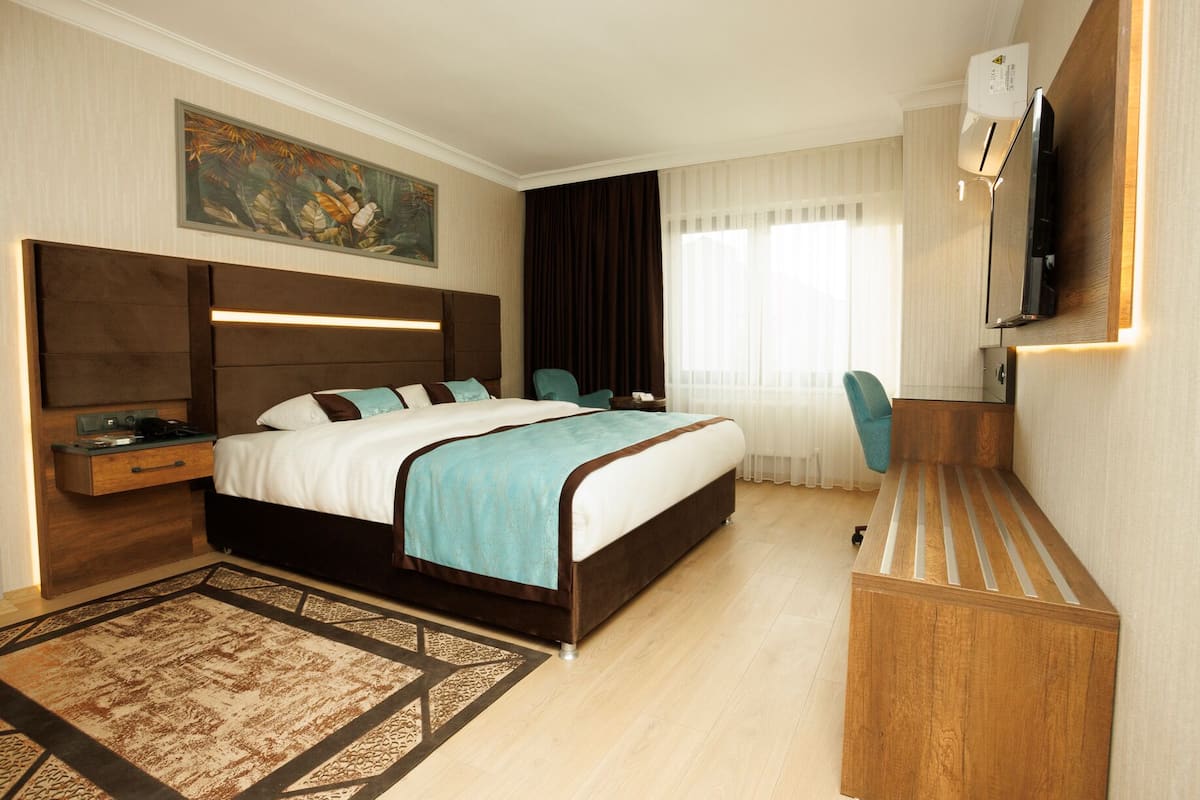A hotel room with a bed, a desk, a chair, a TV, and a painting on the wall.