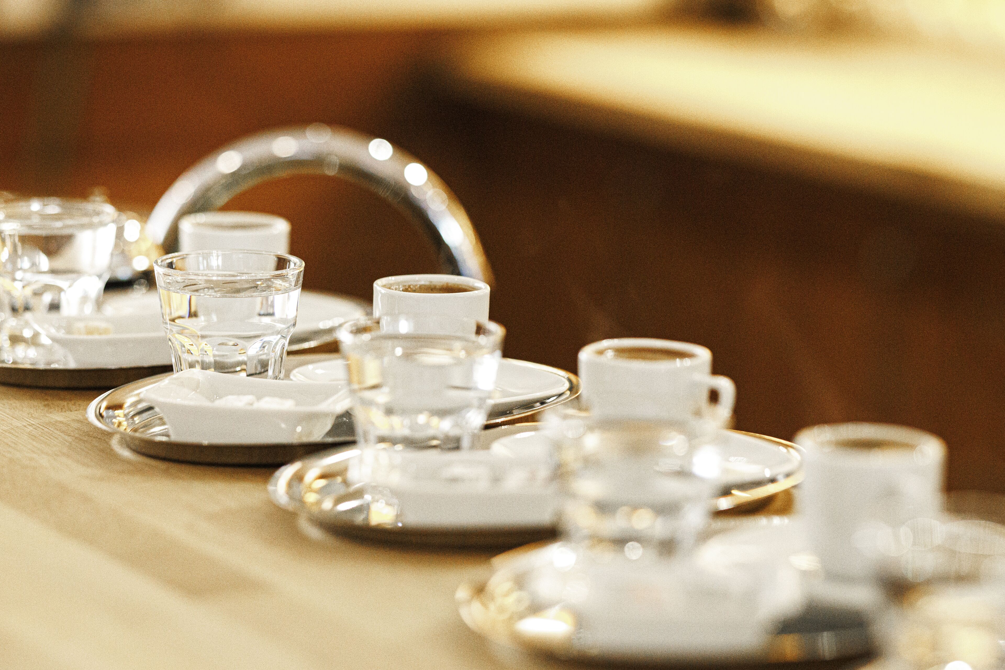 A table set with clear glass cups, saucers, and a teapot, indicating a tea service setup.
