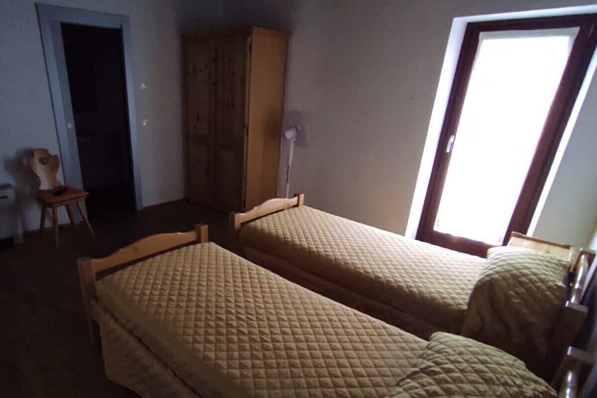 Een kamer met twee eenpersoonsbedden, een houten garderobe, een stoel en een raam met uitzicht.