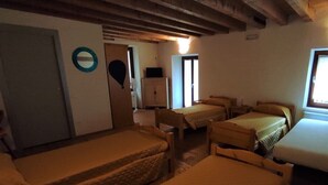 A room with four single beds, a wooden ceiling, a door, and a window. - Ostello Sociale Borgo Venno (Lavenone)