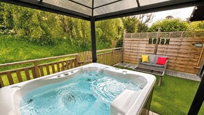 Una bañera de hidromasaje en un área exterior cubierta con una terraza de madera, una valla de madera y un jardín.