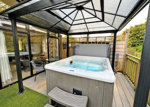A hot tub under a glass-enclosed patio with a wooden deck and a small bench. - 1 bedroom accommodation in Raywell, Beverley (Raywell, Beverley)