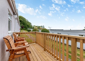 A wooden deck with a bench, a white building, and a view of a green landscape.
