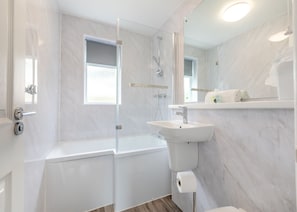 Un baño moderno con ducha envuelta en cristal, un lavabo blanco y un espejo sobre él.