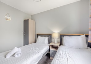 A hotel room with two single beds, a wooden wardrobe, a bedside table with a lamp, and a small decorative item on the wall.