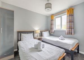 Una habitación de hotel con dos camas individuales, un armario, una mesita de noche con lámpara y una ventana con cortinas.