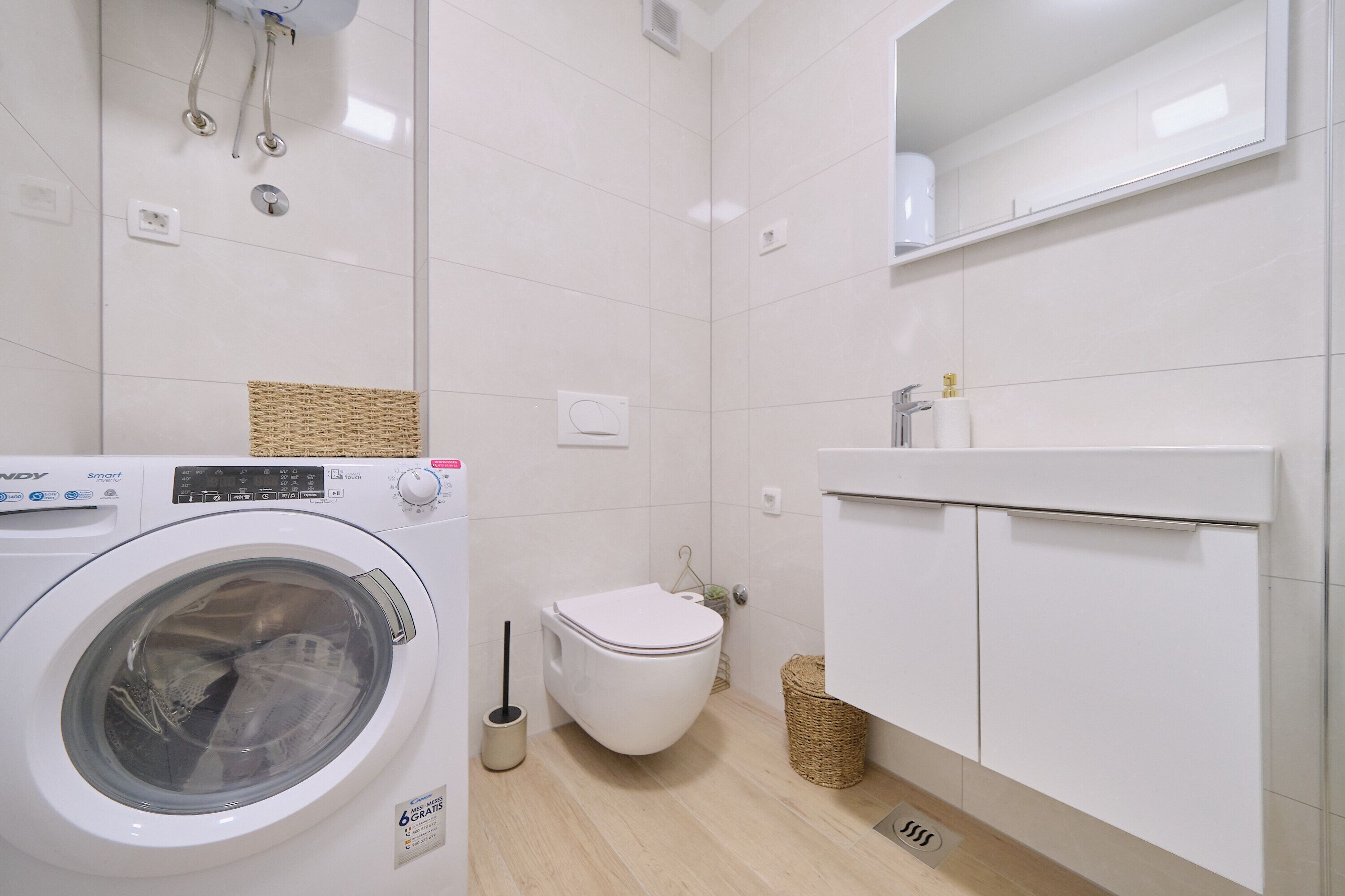 A compact, modern bathroom with a washing machine, toilet, and a cabinet with a mirror.
