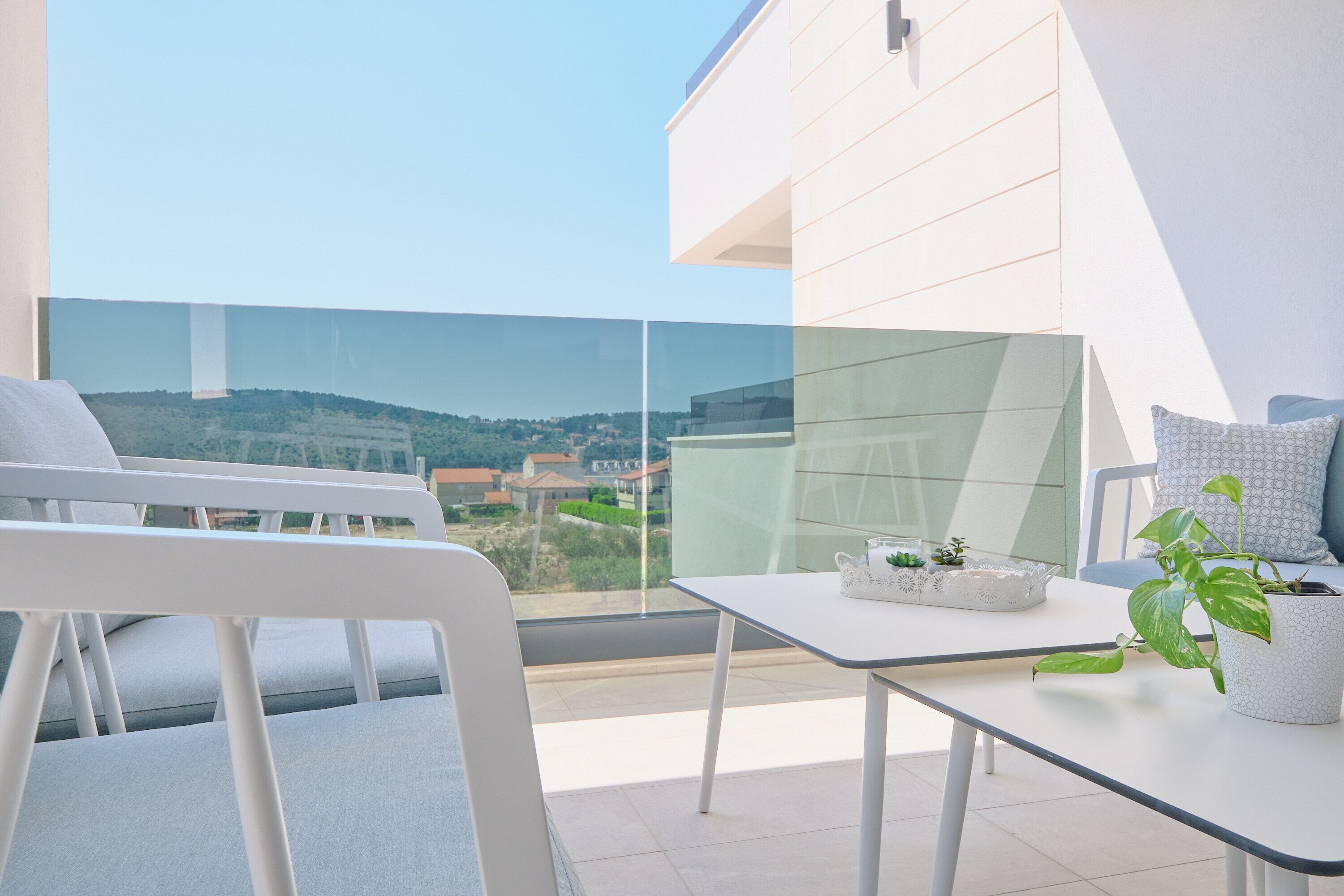 Un balcón moderno con vistas despejadas al paisaje, una mesa blanca con una planta y una silla blanca.
