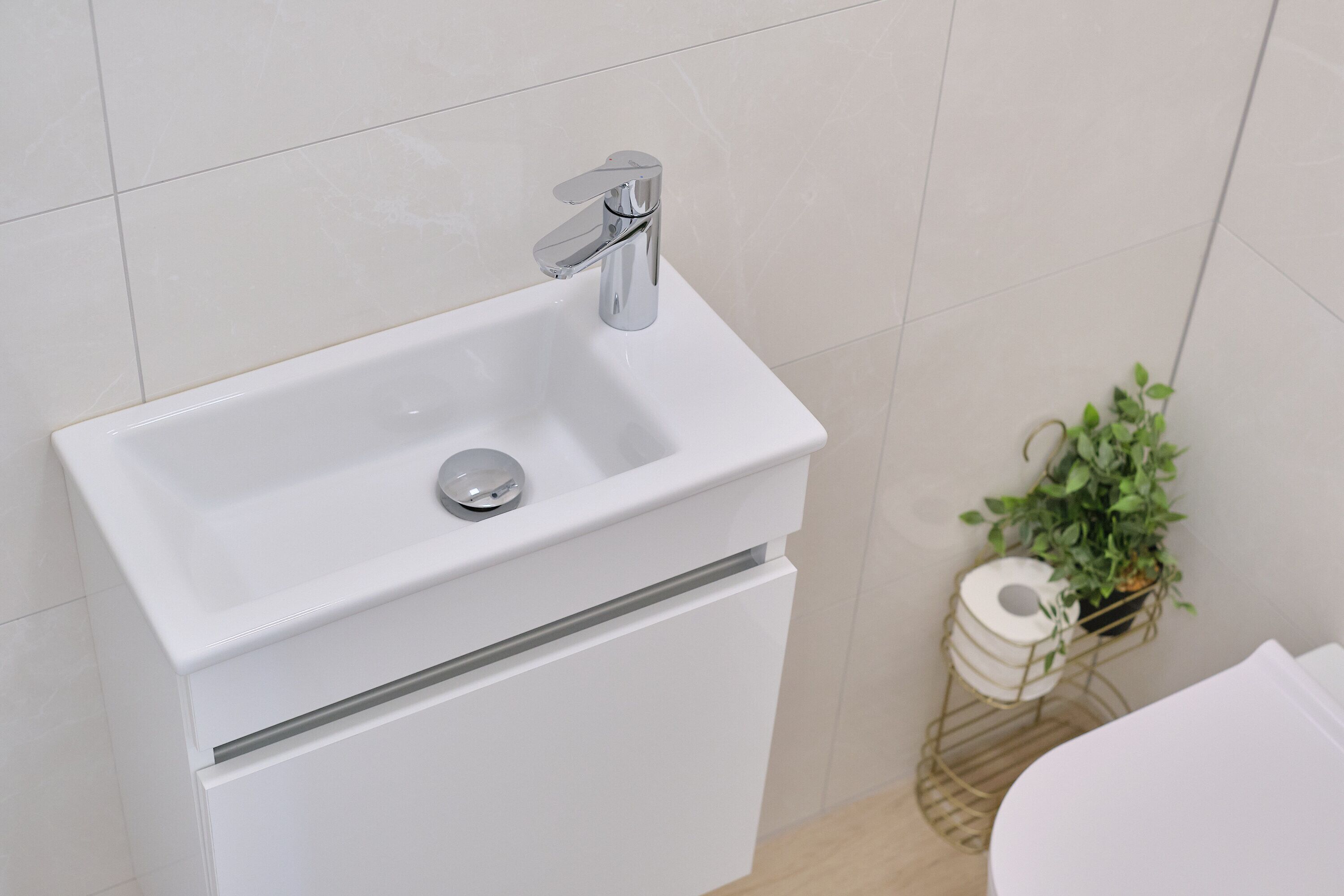A bathroom with a white sink, a modern faucet, and a toilet paper holder with a plant.