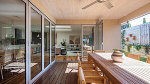 An open-plan living space with a wooden deck, sliding glass doors leading to a kitchen, and a dining area with a large table and chairs. - Luxury and Style on Pasadena with large spa (Rye)