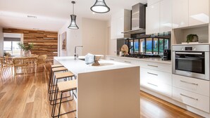 A modern kitchen with a central island, bar stools, stainless steel appliances, and a wooden accent wall. - Luxury and Style on Pasadena with large spa (Rye)