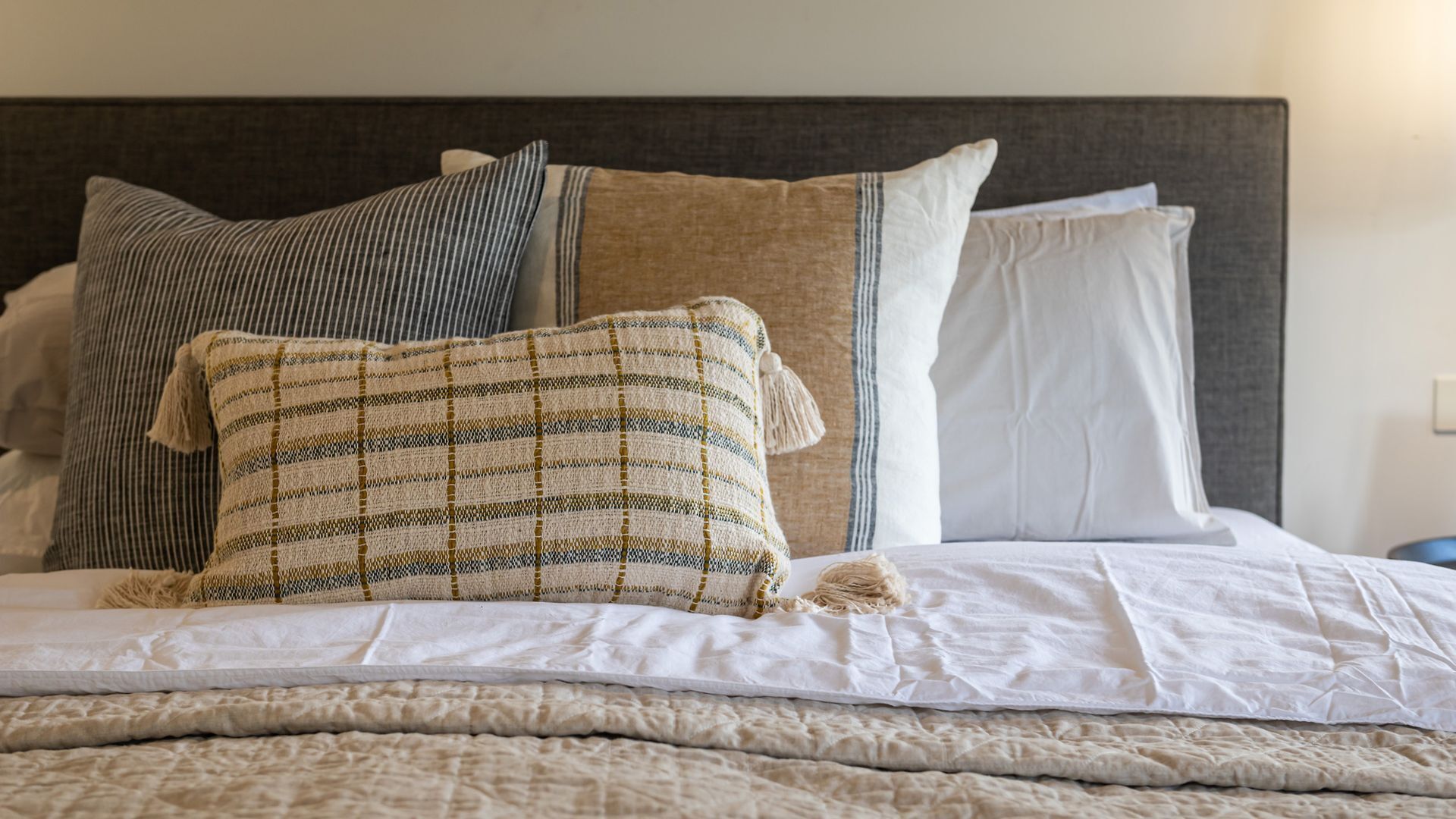 A neatly made bed with a striped pillow, a plain pillow, and a white pillow.