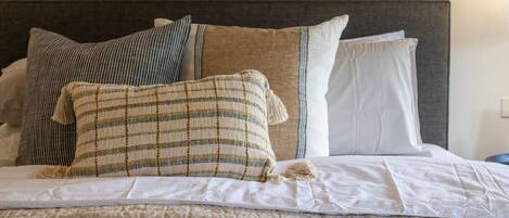 A neatly made bed with a striped pillow, a plain pillow, and a white pillow.