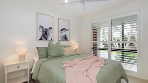 A bedroom with a bed, two bedside tables, a ceiling fan, and a window with blinds. - Stratford by the Sea in Rye (Rye)
