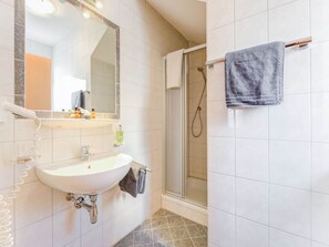 Een badkamer met een wit wastafelmeubel, een spiegel, een douche en een handdoekhouder.