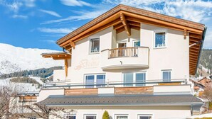 Un immeuble à plusieurs étages doté d’un balcon, offrant une vue sur des montagnes enneigées et un ciel bleu dégagé.